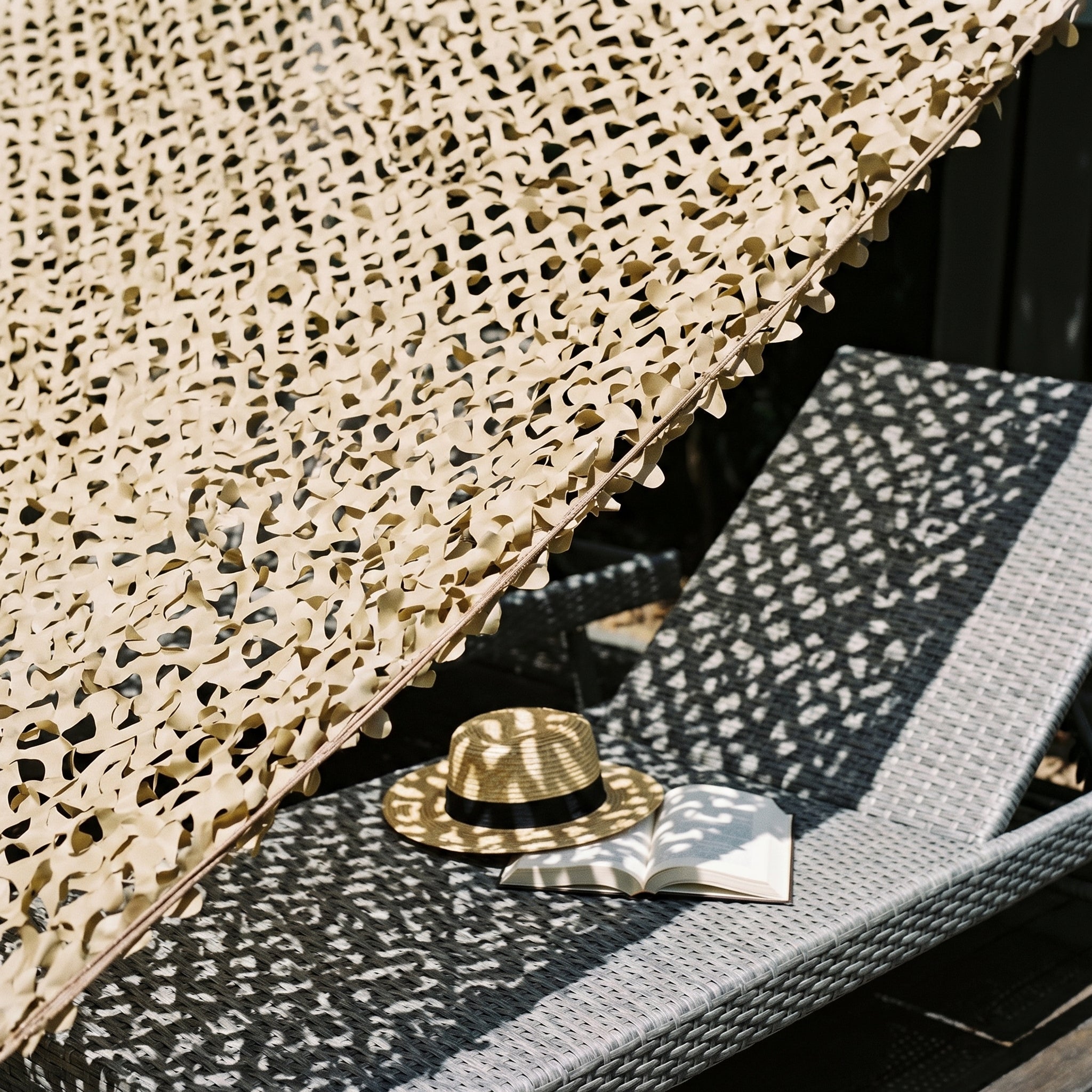 Filet de camouflage brise-vue Camofil couleur sable ombrageant une chaise longue sur une terrasse.