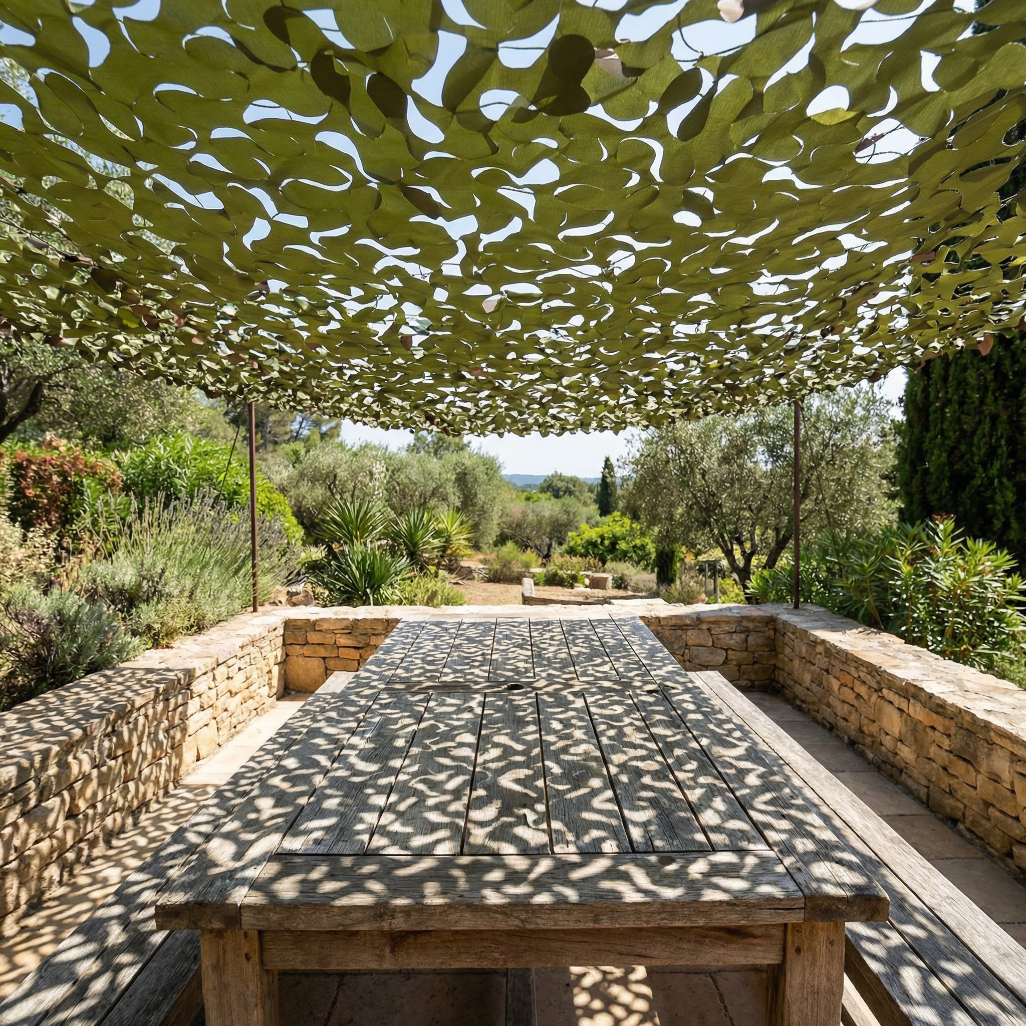 Filet de camouflage renforcé militaire Camofil ombrageant une grande table en bois dans un jardin.