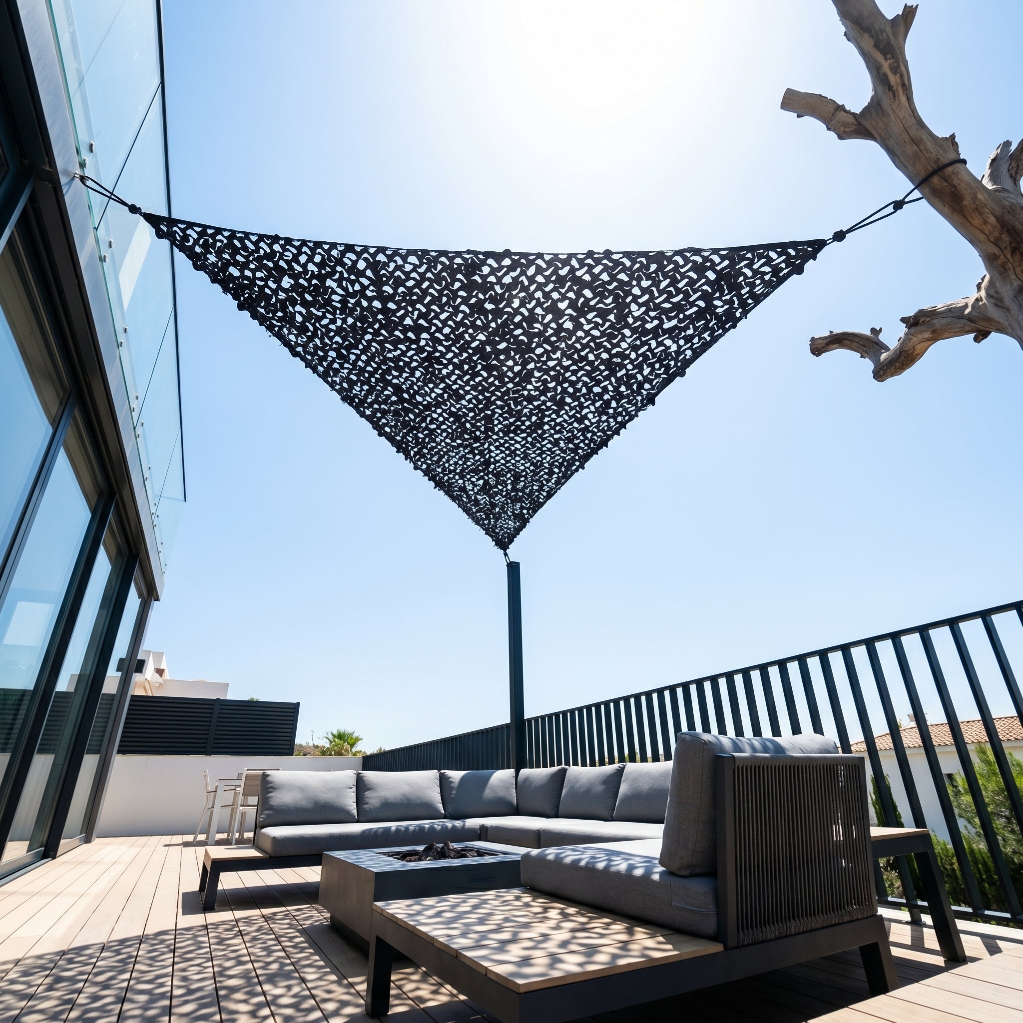 Filet de camouflage triangulaire gris d'angle protégeant un salon de terrasse urbaine du soleil.