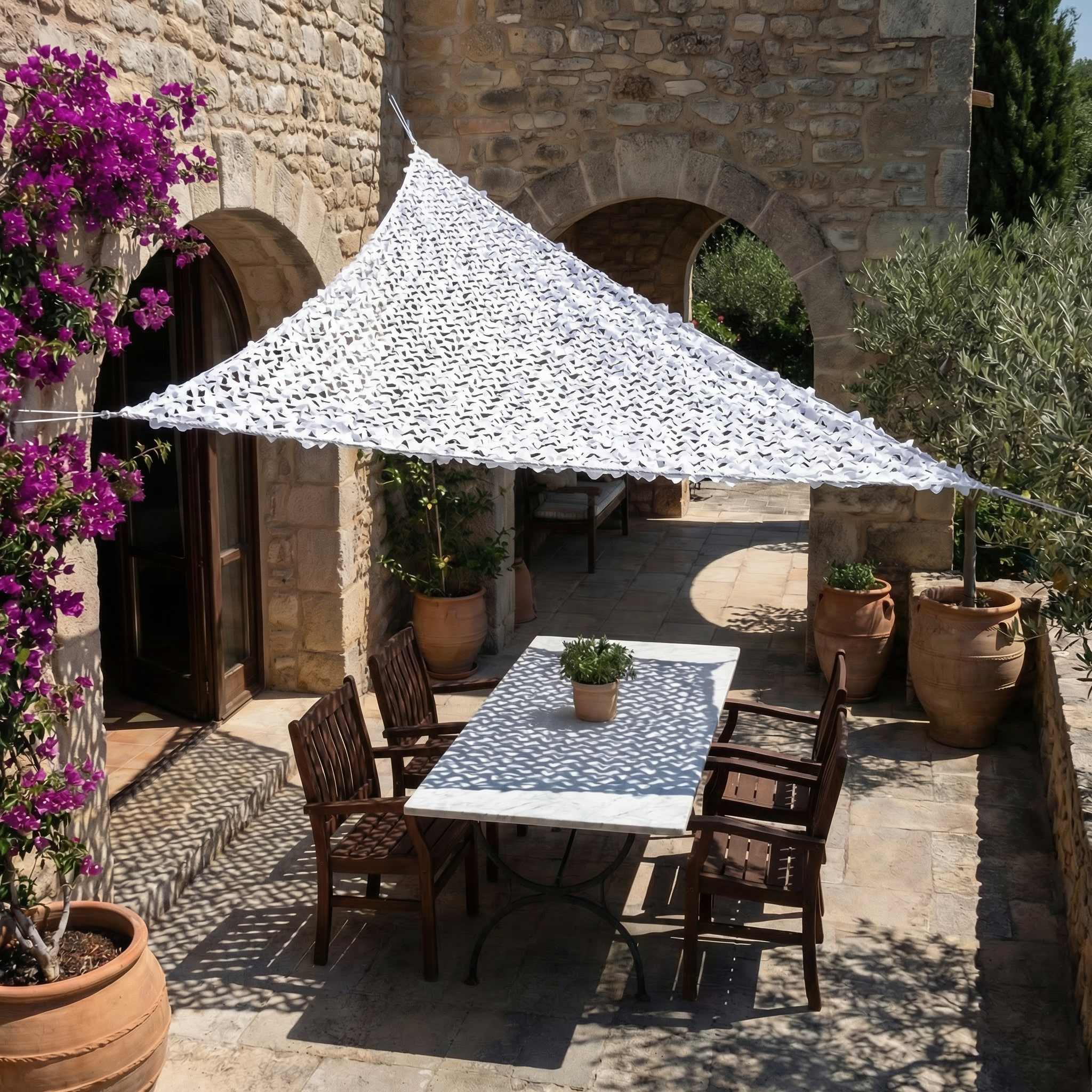 Filet de camouflage triangulaire blanc Camofil ombrageant une table de repas dans une cour en pierre.