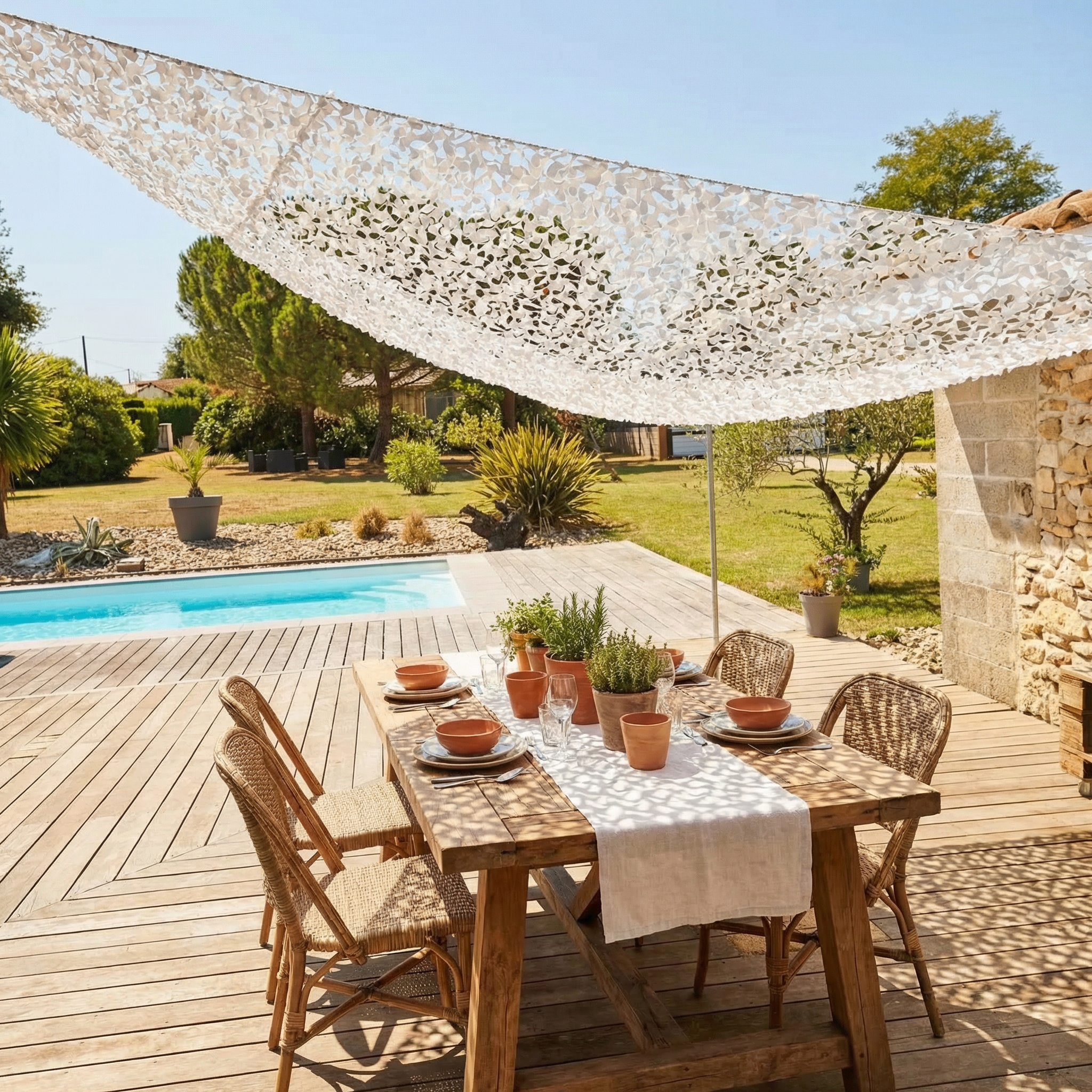 Filet de camouflage triangulaire blanc suspendu près d'une piscine pour abriter un coin repas du soleil.