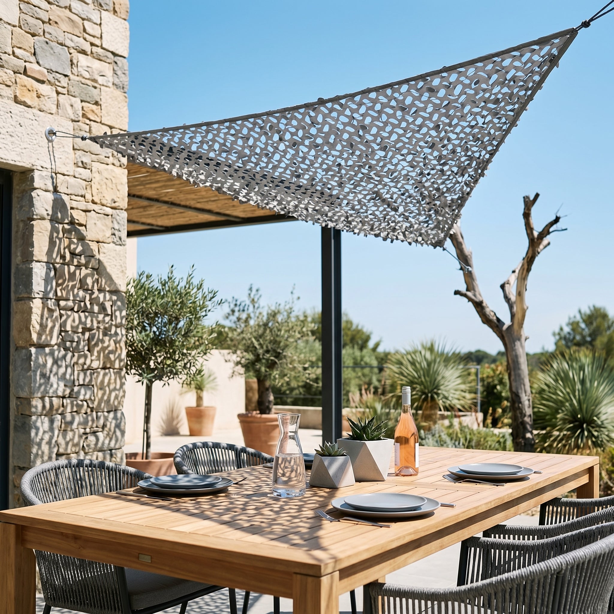 Filet de camouflage triangulaire gris Camofil installé au-dessus d'une table à manger sur une terrasse moderne.