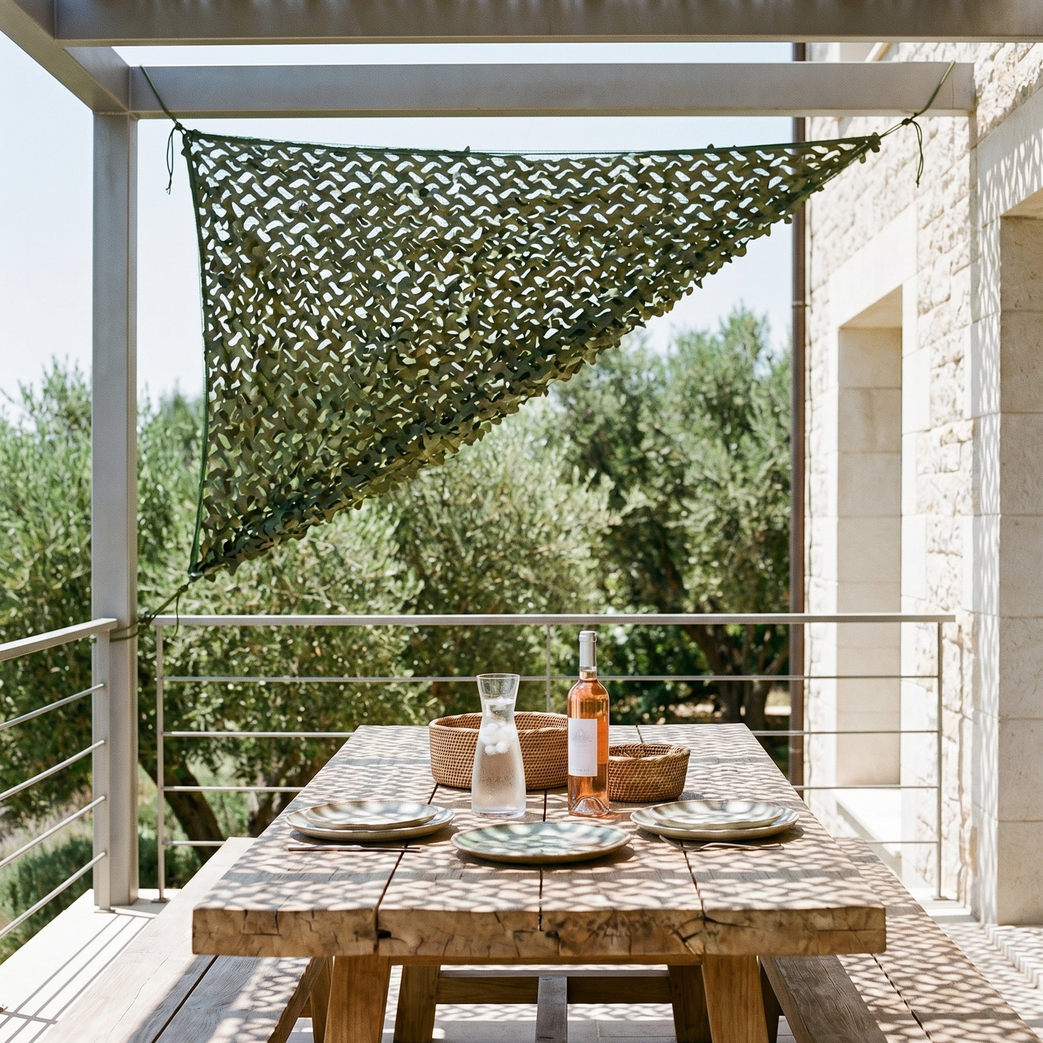 Filet de camouflage militaire d'angle ombrageant une grande table en bois dans un patio arboré.
