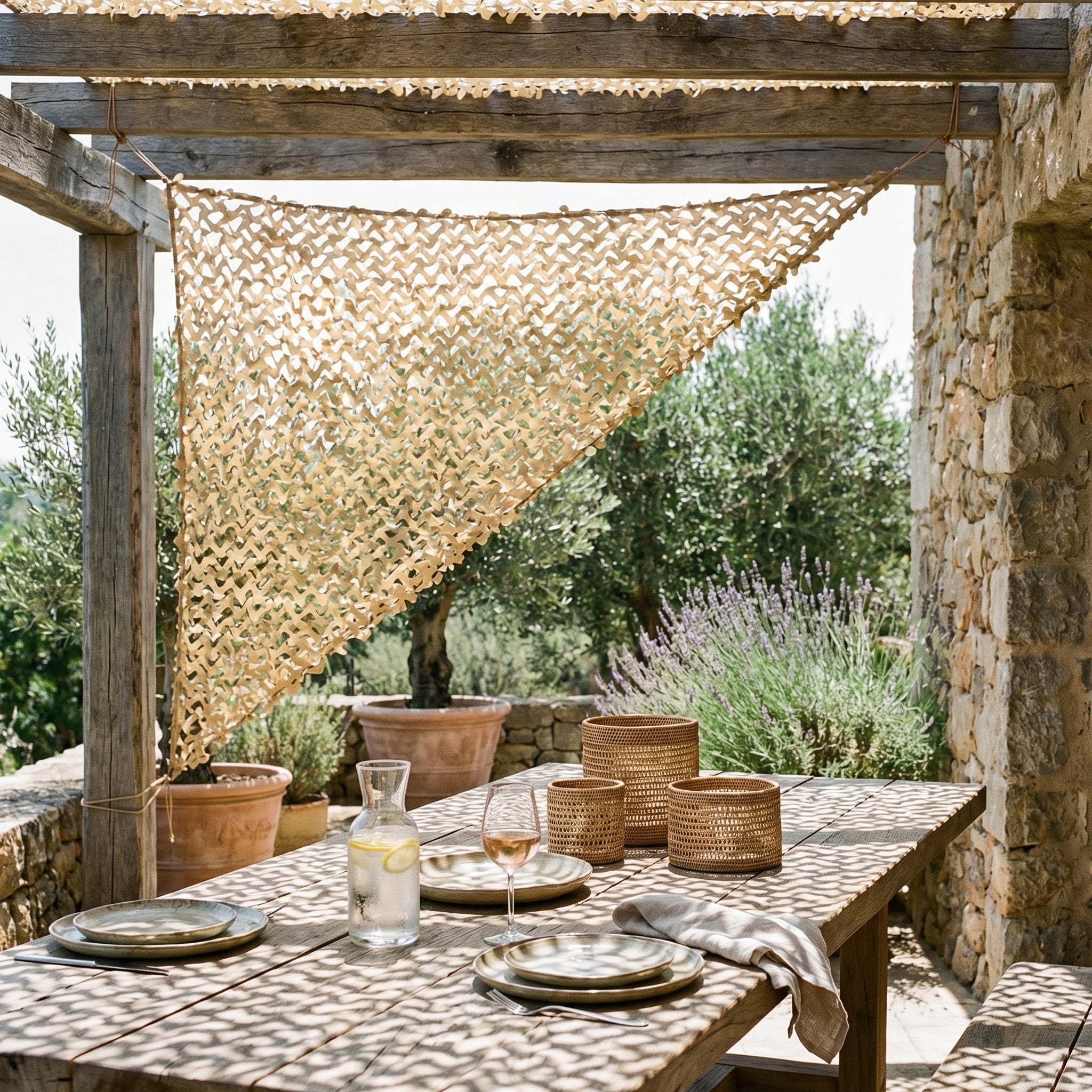 Filet de camouflage triangulaire sable Camofil suspendu pour ombrager une table de repas en terrasse.